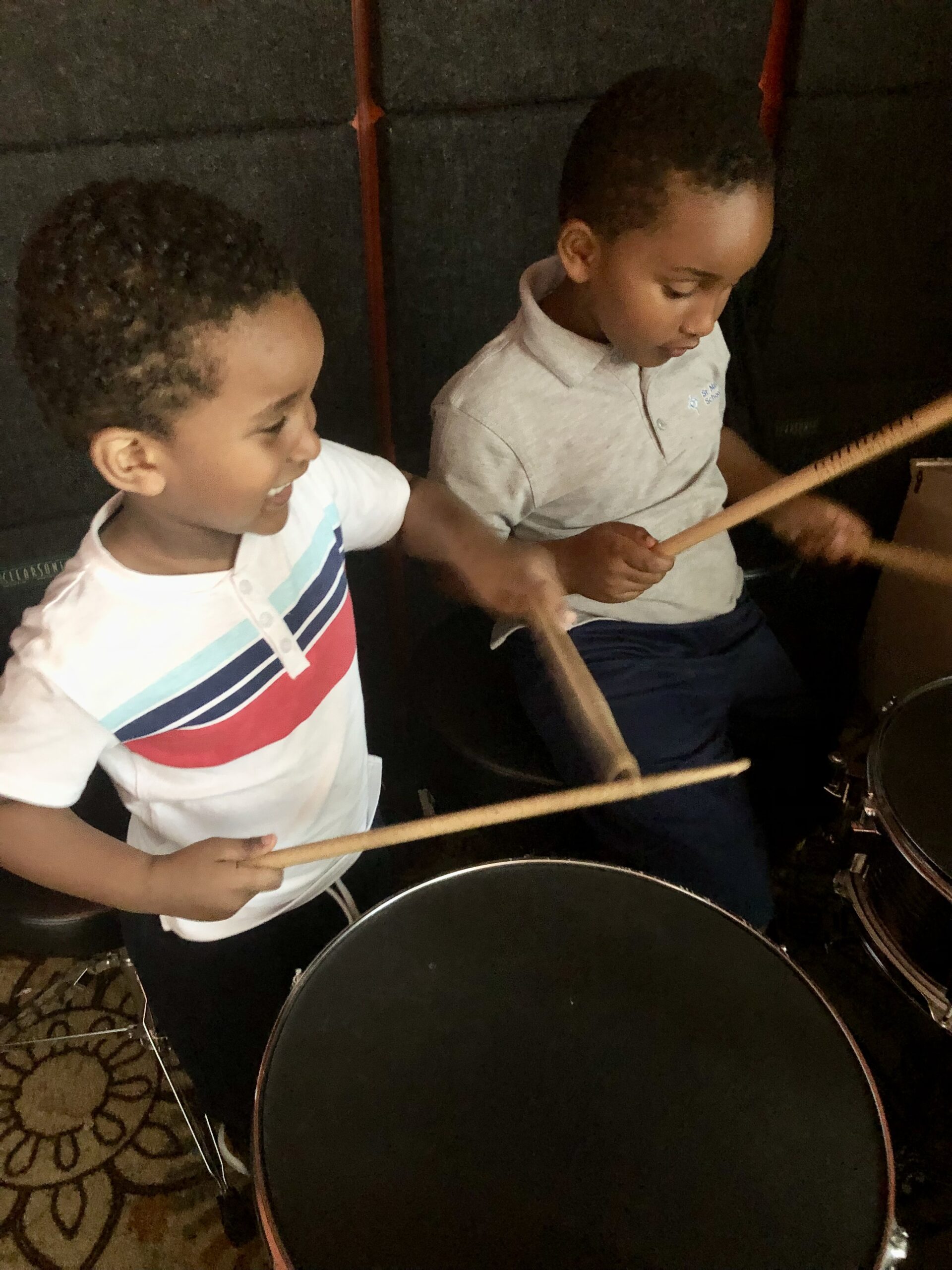 Two children holding drumsticks learning to drum.