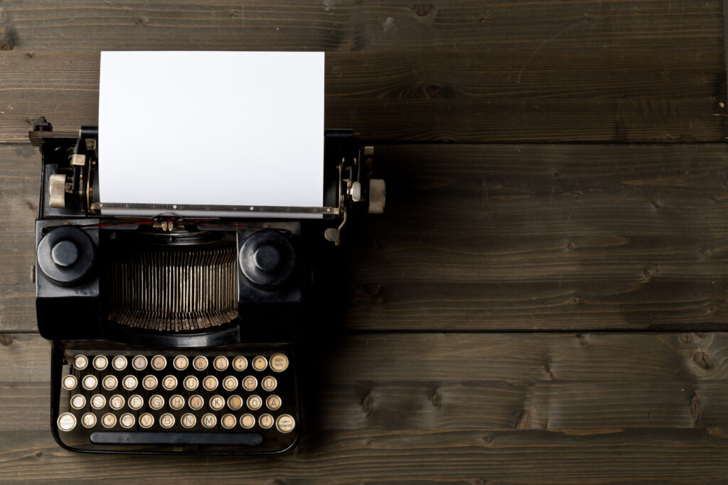 Vintage typewriter top down flatlay shot from above with empty, blank sheet of paper on wood table background
