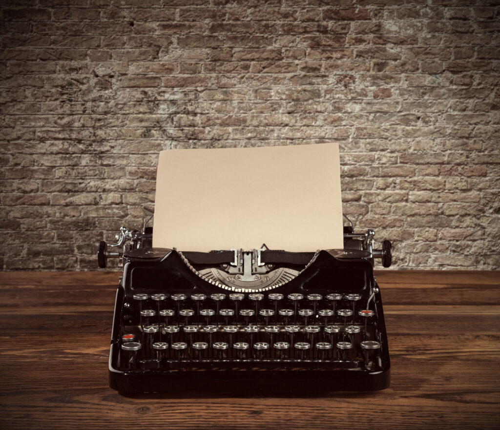 Retro typewriter placed on wooden planks. Old brick wall as background with copyspace.