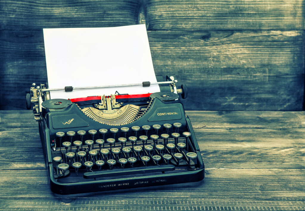 antique typewriter with white paper page on wooden table. vintage style toned picture